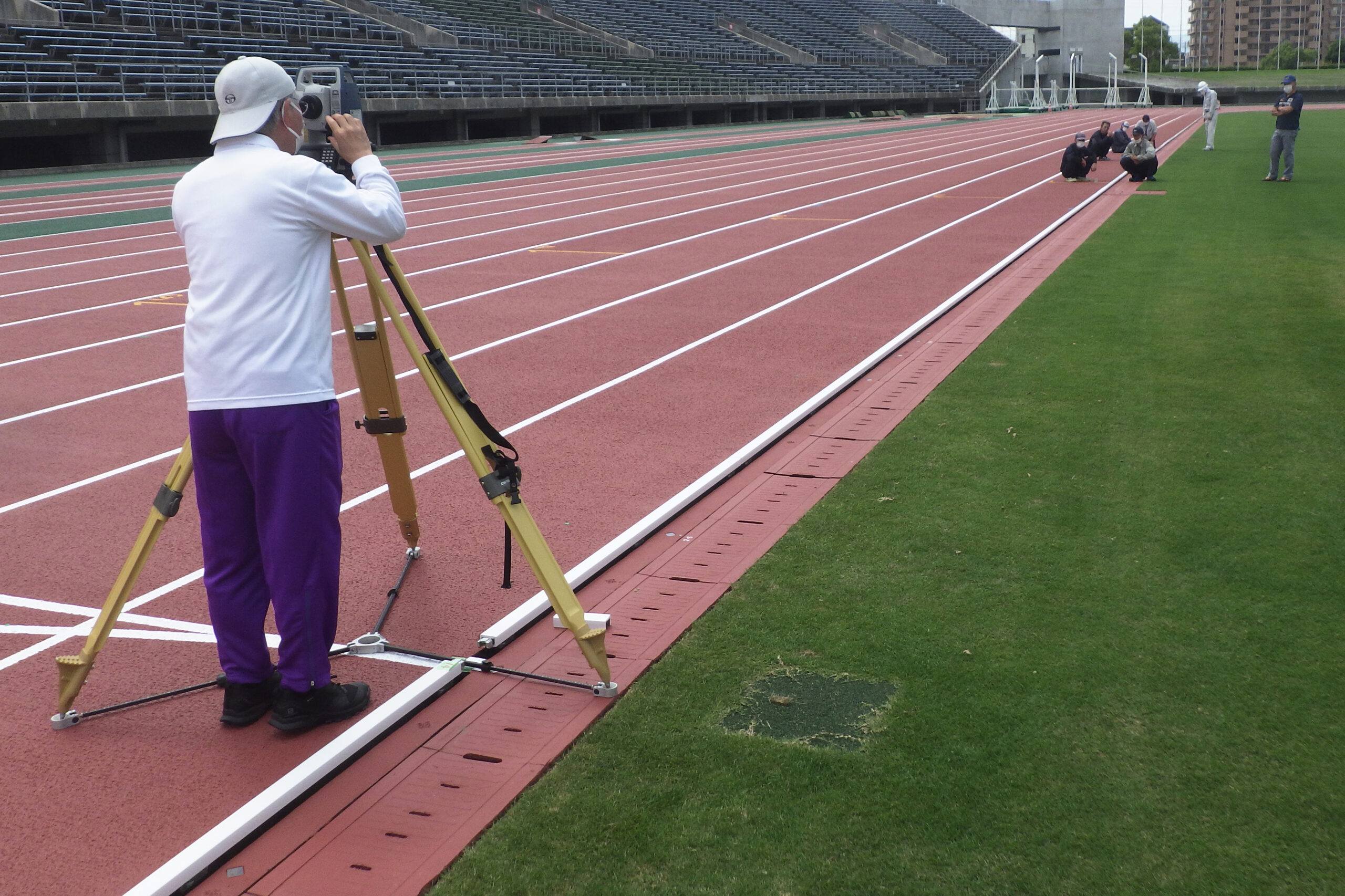 陸上トラックの公認検定において、トータルステーション（光波測量機）で距離や位置を測定している様子